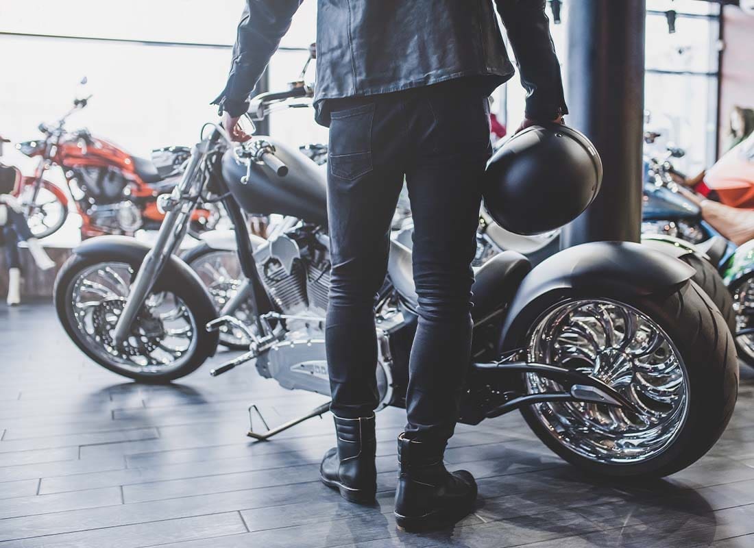 Motorcycle Dealership Insurance - View of Man From Behind Holding a Motorcycle Helmet and Looking at a Motorcycle in a Dealership Shop